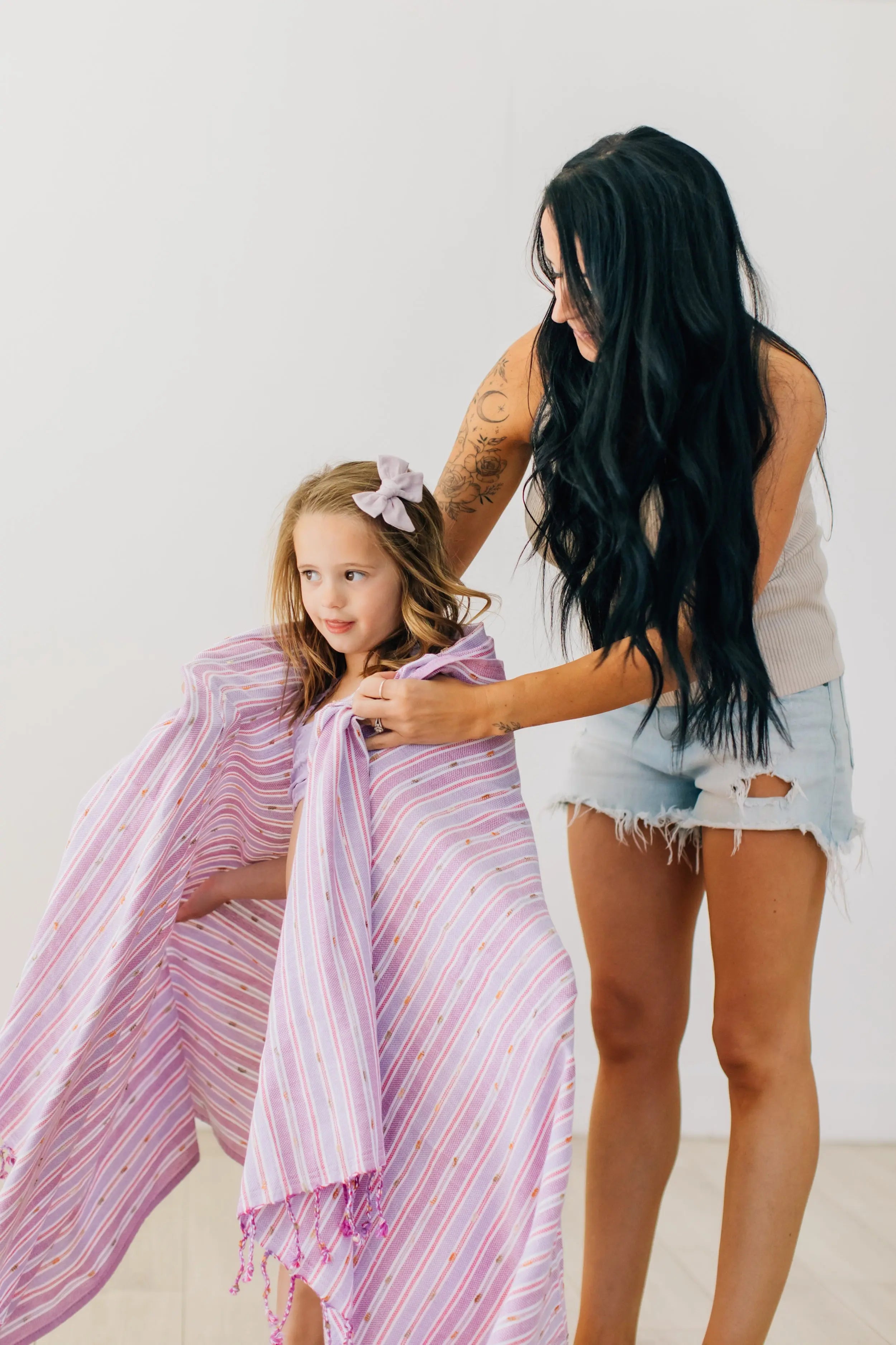 mom wrapping daughter in stripe purple and pink with pom pom turkish towel , hand tied tassels . beach and bath towel 