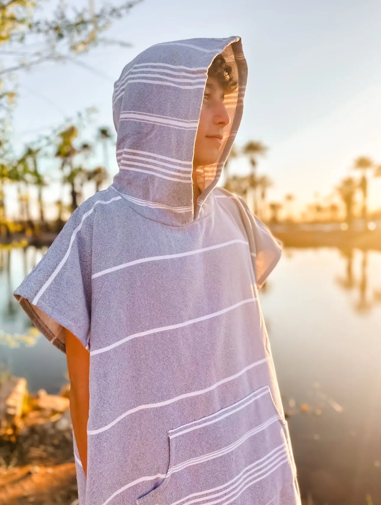 Teenage boy side view in gray stripe turkish surf poncho , hooded turkish towel 