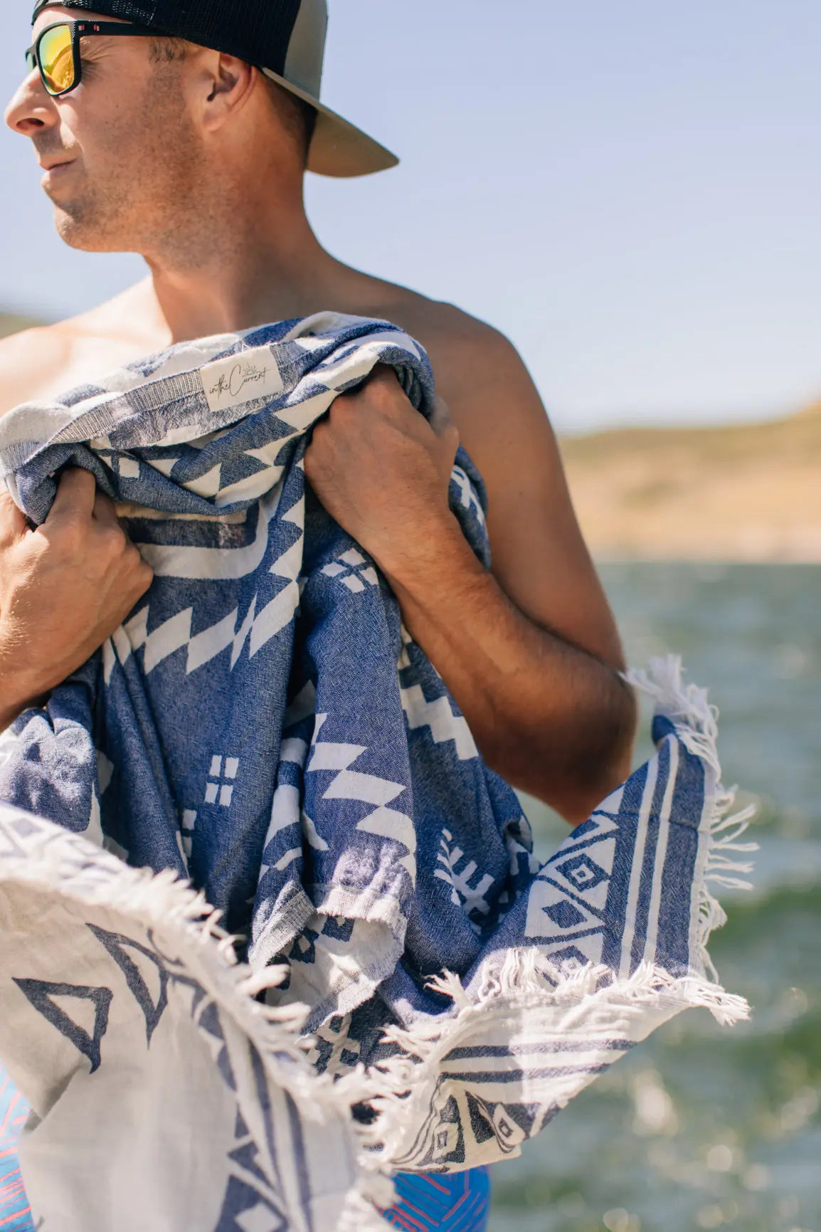 man holding towel on surf boat summertime -navy blue reversible pattern turkish towel diamond pattern 