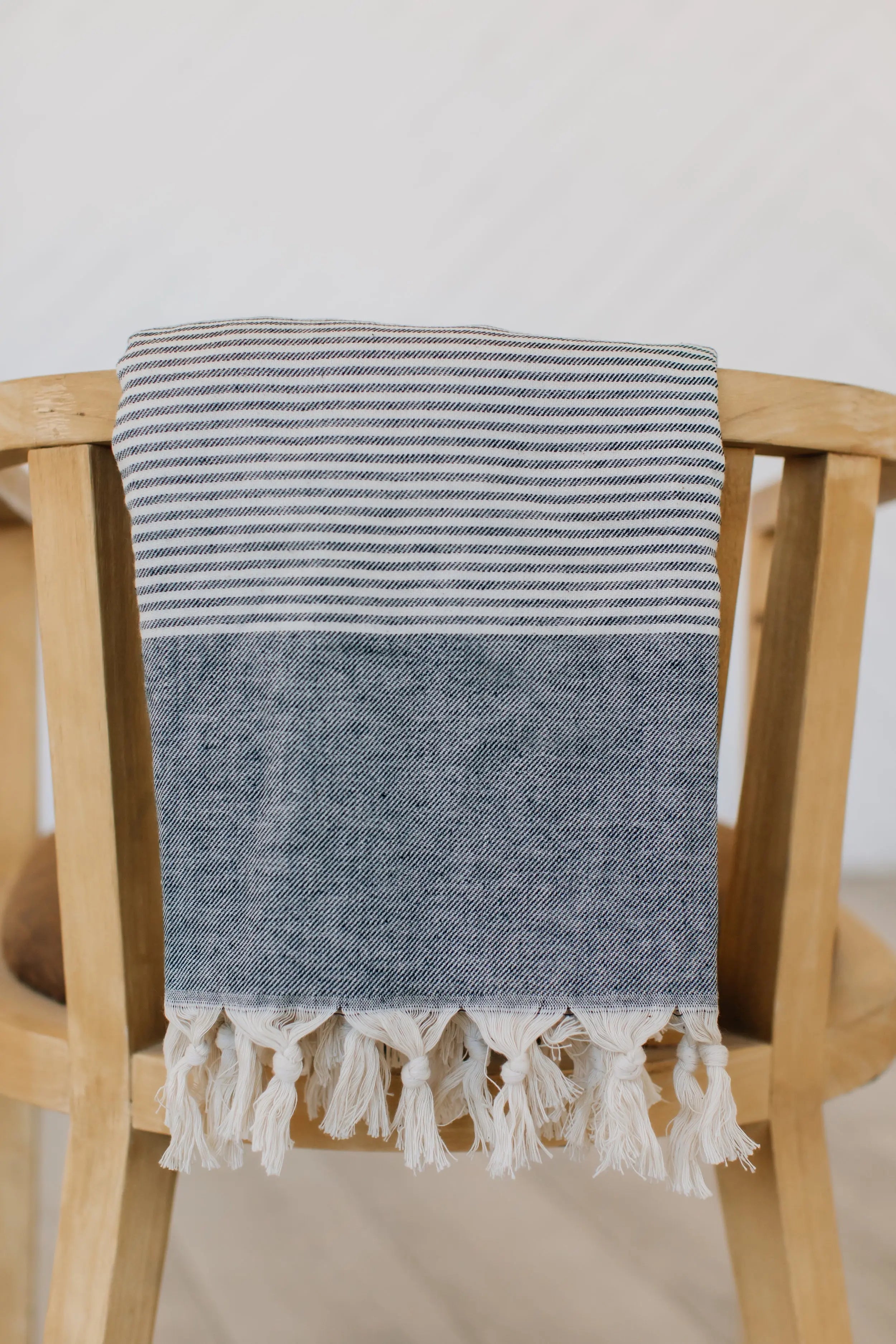 gray soft turkish towel with stripes and hand tied tassels, draped over chair 